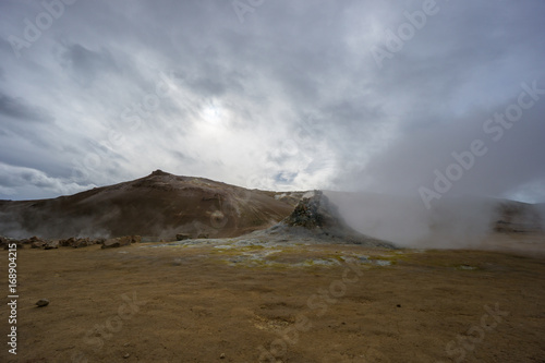 Iceland - Active fumarole pushing gas and hydrogen sulfide out of the yellow colored ground in front of brown volcano