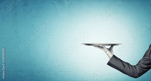 Hand of butler holding empty metal tray against blue background