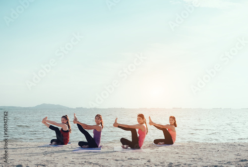 Young group man and woman yoga practice on mat relaxation in class exercise with pose fitness sport for healthy on the beach and seaside modern city at sunrise relax