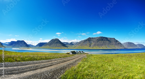 Travel to Iceland. beautiful sunrise over the ocean and fjord in Iceland. Icelandic landscape with mountains, blue sky and green grass on the foreground. View of the road to houses in the north-west