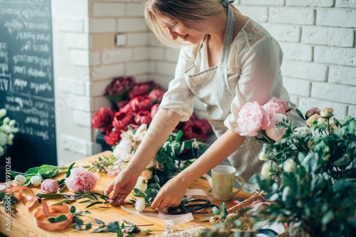 Smiling lovely young woman florist arranging plants in flower shop