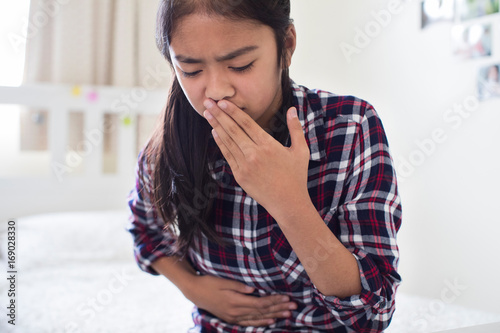 Young Girl Sitting On Bed At Home Feeling Nauseous