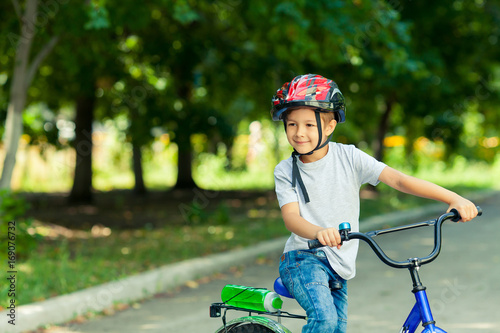 Little boy learns to ride a bike in the Park near the home. Portrait of a cute kid on bicycle. Happy smiling child in helmet riding a cycling.