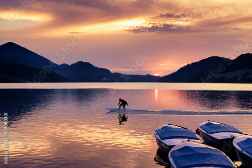 Sunset at Lake Fuschl with silhouette of a man riding an electric surfboard, boats in foreground, Fuschl am See, Fuschlsee, Salzburg state, Salzkammergut, Austria, Europe