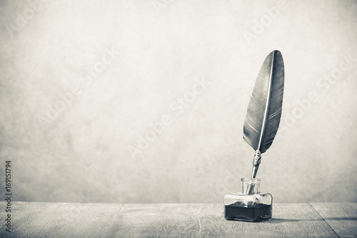 Quill pen with inkwell on wooden desk. Vintage old style sepia photography