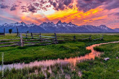 Golden Fiery Sunset at Grand Teton - A colorful spring sunset at Teton Range, seen from an abandoned old ranch in Mormon Row historic district, in Grand Teton National Park, Wyoming, USA. 