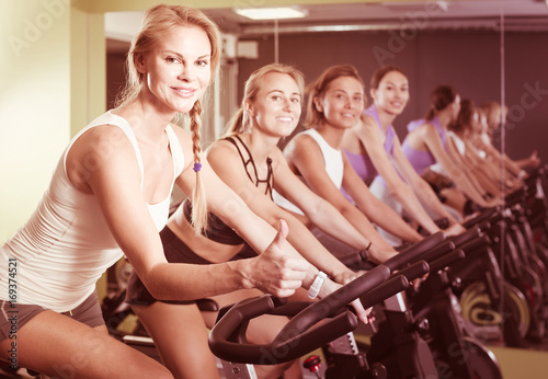 Portrait of women on exercise bike gesturing thumbs up at gym