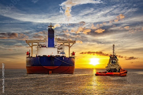 Tanker and tugboat on sea at sunset.