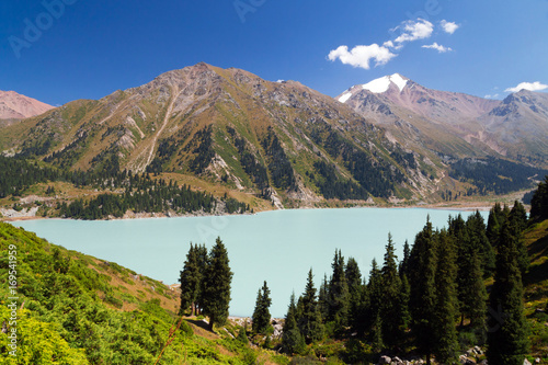 Big Almaty lake. View of a lake in the mountains. Snow-capped peak in the background. Sunny summer afternoon.
