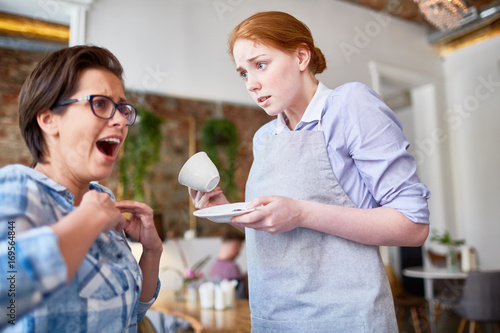 Clumsy waitress spilled hot tea from cup on her client