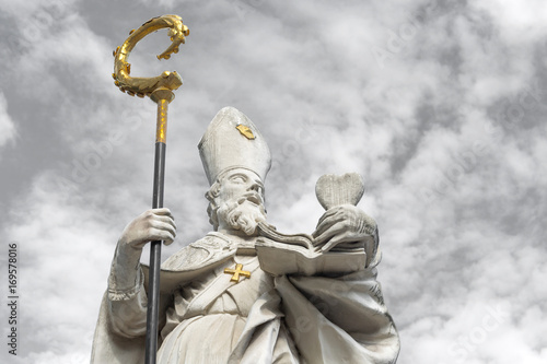 White marble sculpture of Saint Augustine with golden cross and bishop's crook, holding a heart in his left hand