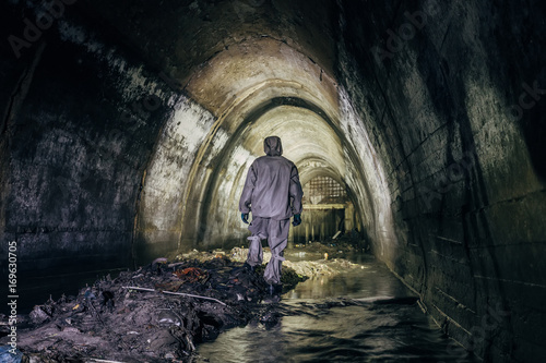 Sewer tunnel worker in chemical protective suite in underground gassy sewer tunnel 