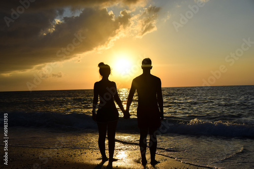 giovane coppia che si tiene per mano in spiaggia durante il tramonto 
