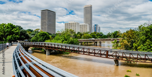 Panorama high and fast water rising in Bayou River from Rosemont pedestrian bridge with near town Houston in background, cloud blue sky. Heavy rains of Harvey Tropical Hurricane storm cause many flood