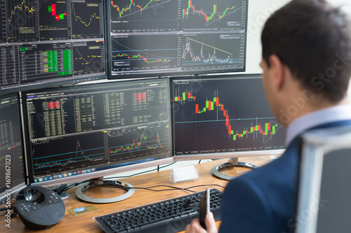 Over the shoulder view of computer screens ful of charts and data analyses and stock broker trading online.