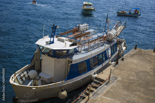 Piccola nave bianca ancorata alla banchina. Si tratta di un peschereccio adibito appunto alla pesca in mare. Dietro altre piccole barche si avvicinano al golfo.