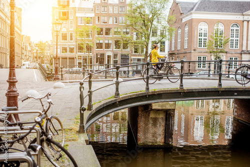 Cityscape view on the water channel and bridge with young woman riding a bicycle during the morning in Amsterdam city