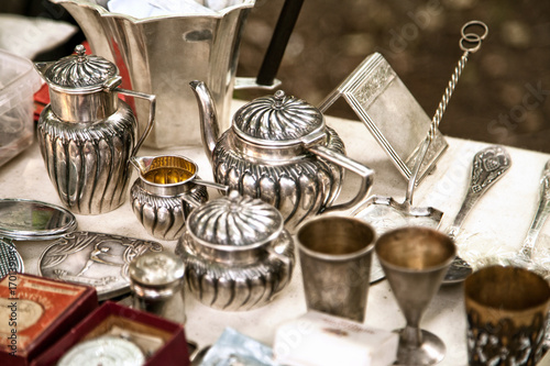 Antique silver teapots, creamer and other utensils at a flea market. Old metal tableware collectibles at a garage sale