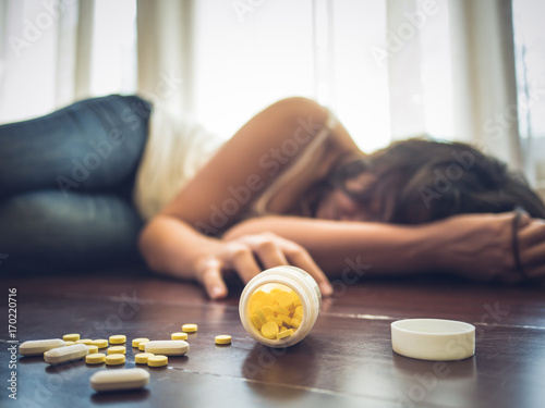 Woman taking medicine overdose and lying on the wooden floor with open pills bottle. Concept of overdose and suicide.