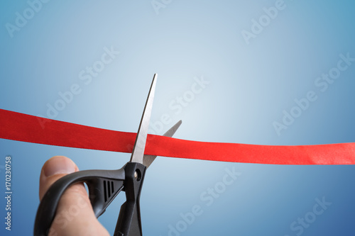 Scissors are cutting red ribbon. Opening ceremony concept. Isolated on blue background.