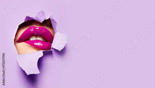 Beautiful plump bright lips of pink color peep into the slit of colored paper.