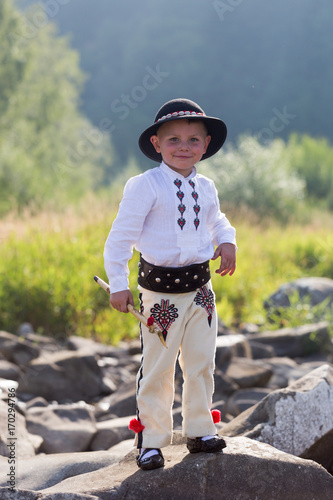 Smiling child boy in traditinal Polish mountain outfit and black hat stands on mountain rocks