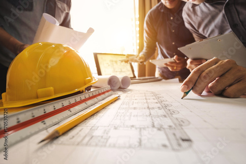 Three colleagues discussing data working and tablet, laptop with on on architectural project at construction site at desk in office 