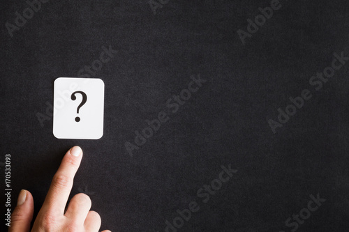 Finger pointing to the sign of question on the black background. Solution search concept. Empty place for a text.