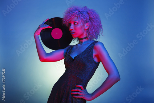 millennial black woman with groovy hair holding an old eighties vinyl with retro disco lights