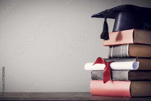 Graduation hat and diploma with book on table