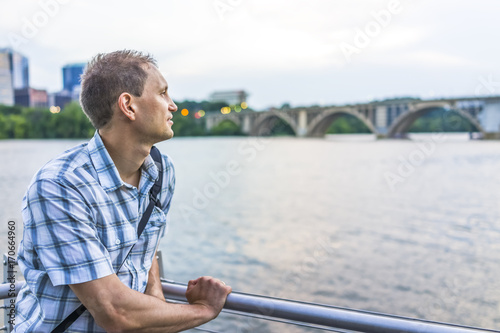Young man looking over potomac river with Francis Scott Key Bridge during sunset