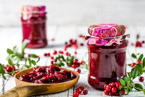 Jars of jam with cranberry on white wooden background