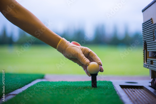 Woman golfer's hand holding ball on tee with golf course background. close up of golf players hand placing ball on tee at driving range in sport club.
