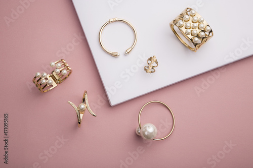 Perłowe złote bransoletki i pierścionek na różowym i białym tle
