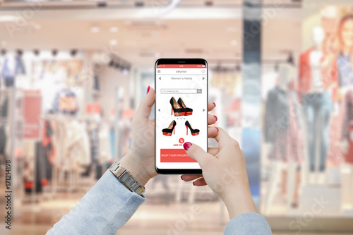 Girl purchasing shoes on her smartphone in front of boutique