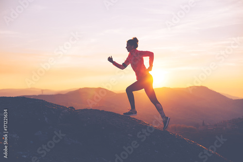 Athletic girl finishes a run in the mountains at sunset. Sport tight clothes. Intentional motion blur.