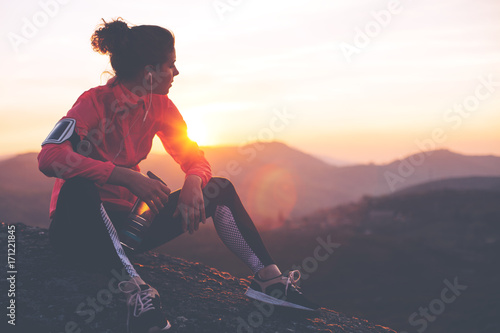 Sportowa kobieta odpoczywa po ciężkiego szkolenia w górach przy zmierzchem. Sportowe ciasne ubrania.