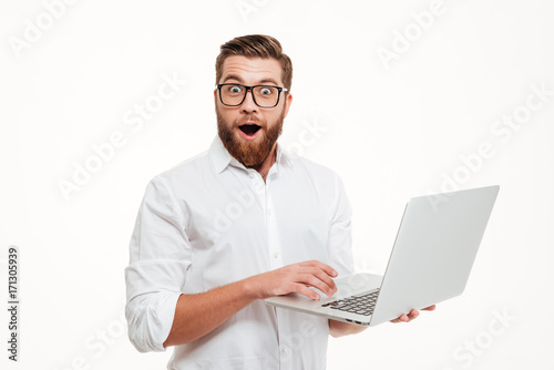 Shocked young bearded man using laptop.
