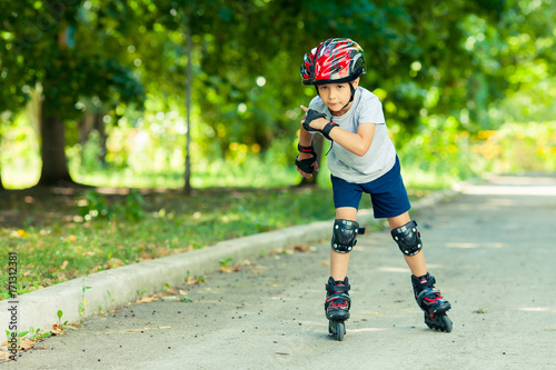 Little boy riding on rollers in the summer in the Park. Happy child in helmet learning to skate.