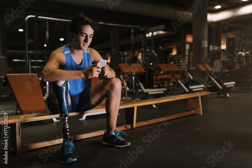 Disabled young man using his mobile in the gym.