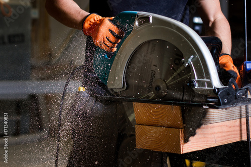 Close-up of carpenter using electric circular saw to cut wood planks