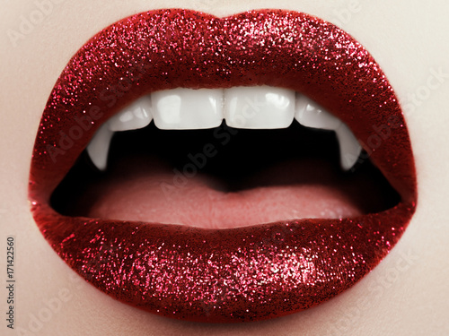 Female lips with glittering red lipstick, vampire teeth