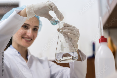 Low-angle view of the hands of a successful chemist smiling while mixing two liquid chemical substances during an innovative experiment in an industrial lab