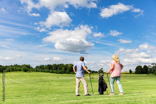 Active senior couple playing golf on a course.