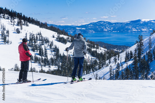 Two middle aged men on skis look out over the lake tahoe mountains
