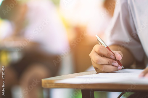 Closeup to hand of student holding pen and taking exam in classroom with stress for education test .