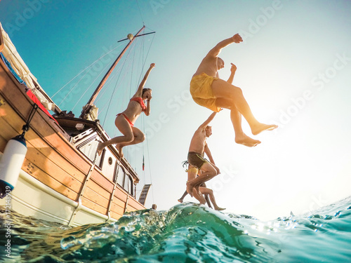 Happy friends diving from sailing boat into the sea - Young people jumping inside ocean in summer excursion day - Vacation, youth and fun concept - Main focus on left man - Fisheye lens distortion