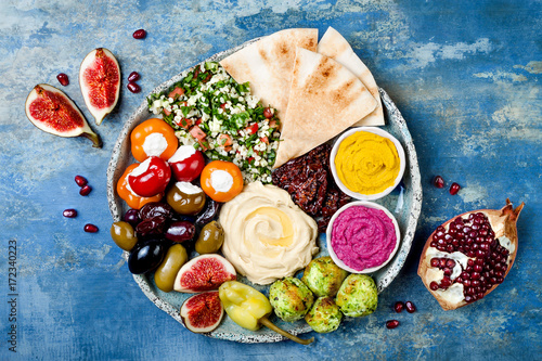 Middle Eastern meze platter with green falafel, pita, sun dried tomatoes, pumpkin and beet hummus, olives, stuffed peppers, tabbouleh, figs. Mediterranean appetizer party idea