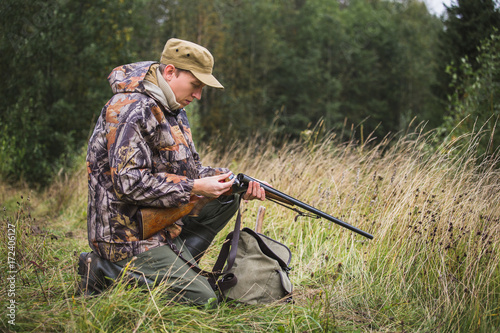 Hunter with a backpack and a hunting gun in the autumn forest. Man is charging a hunting rifle. 