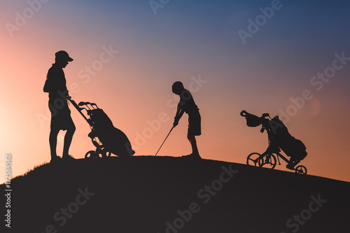 silhouettes of man with his son golfers playing golf on golf course at sunset